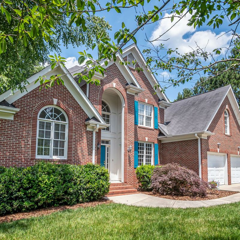 A red-brick two-story house with arched windows and a green lawn