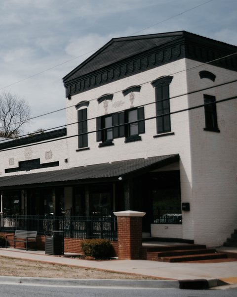 The white two-story brick commercial building on 2nd Avenue in downtown Dacula, with black trim and a covered porch
